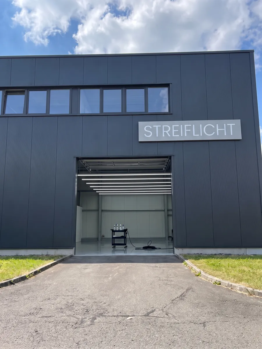 Halle mit dunkler Metallfassade und dem Schild Streiflicht. Das Tor steht offen, drinnen helles LED-Licht und ein Wagen mit Pflegemitteln.